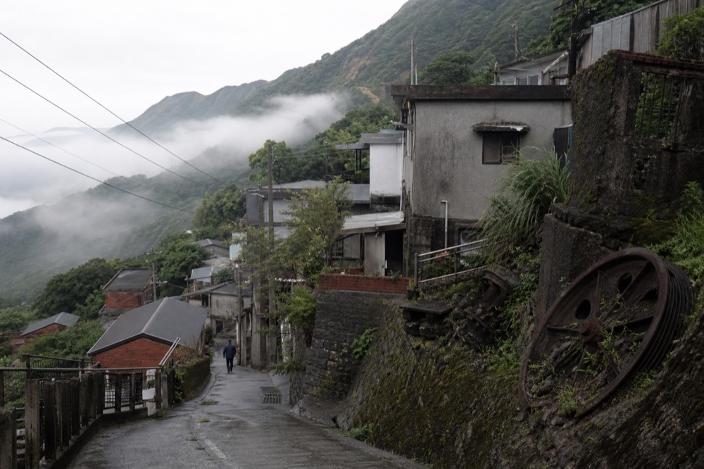 Stone mining village buildings on a green hillside above a narrow coastal valley