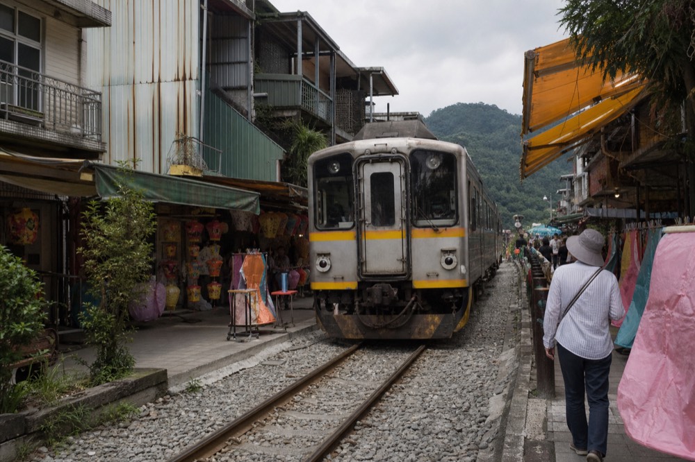 A Pingxi branch train pulling into Shifen station, with old street stalls visible through the window