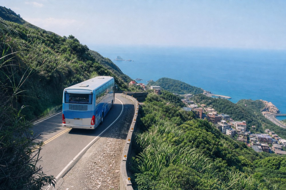 A scenic view from a tour coach winding through mountains near Jiufen, with the sea in the distance