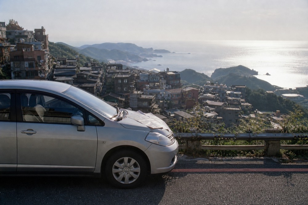A private car at a viewpoint overlooking the Northeast Coast, with Jiufen's hilltop buildings in the background