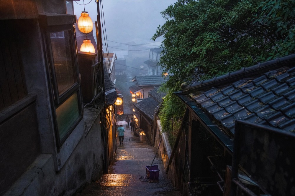 An emptying old street in early evening with lantern light reflecting on wet stone steps
