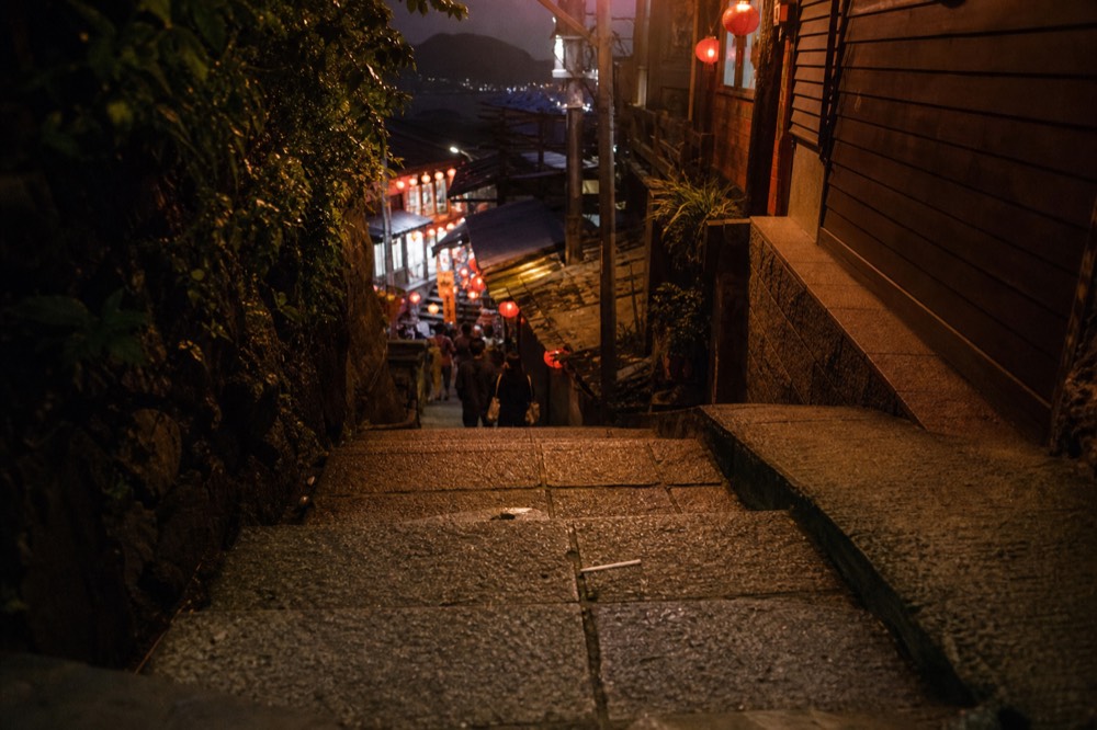 A lit old street seen from above with lantern glow spilling onto stairways