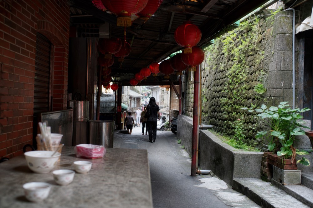 A narrow covered alley between old brick shopfronts with red lanterns overhead