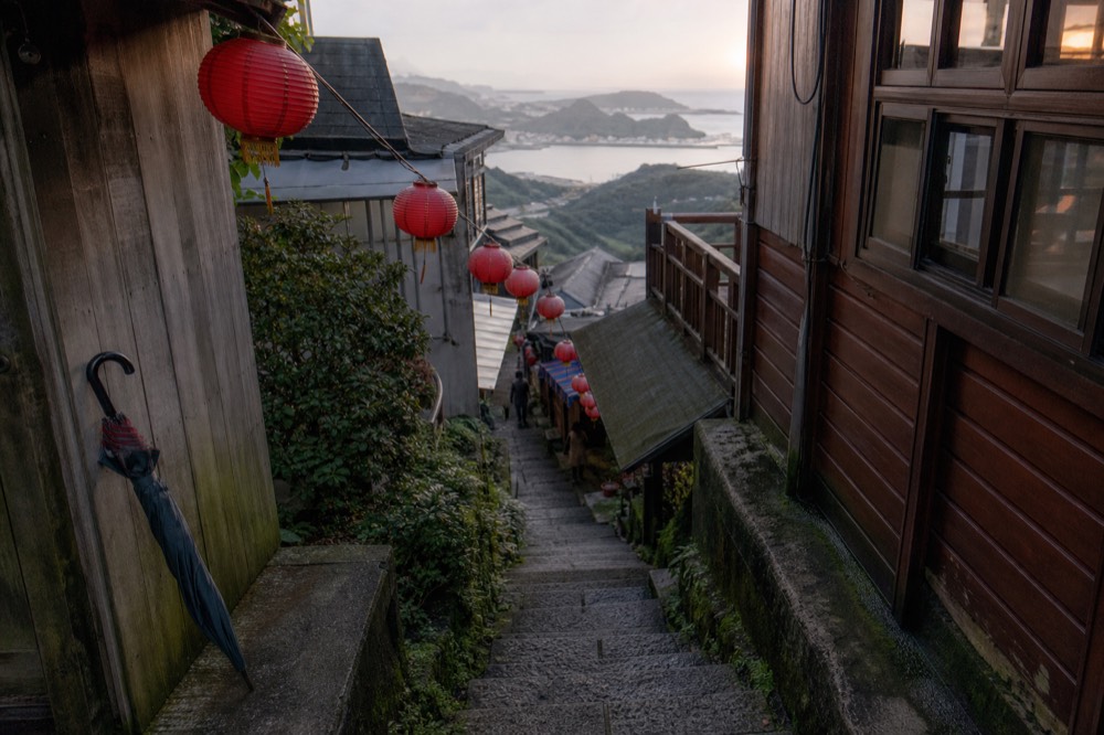 Steep stone steps between wooden teahouse buildings with red lanterns descending a hillside