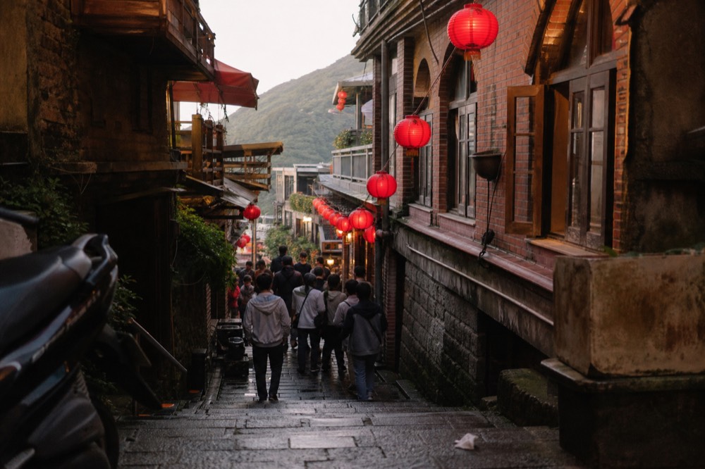 A crowd of visitors walking through a narrow lantern-lit old street in the late afternoon