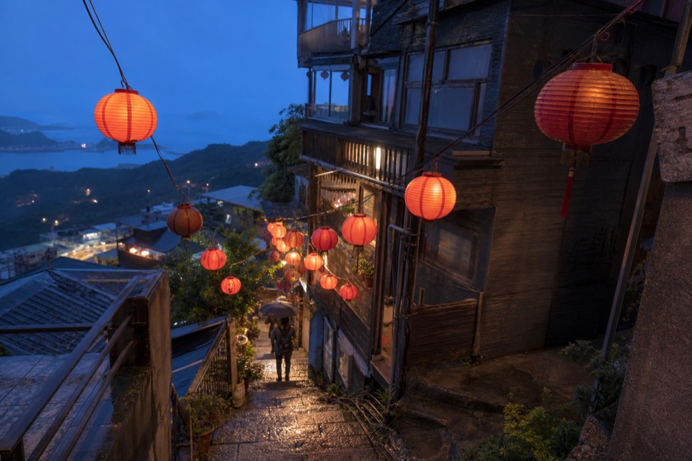 Red paper lanterns glowing along a steep lane as blue hour settles over a hillside town