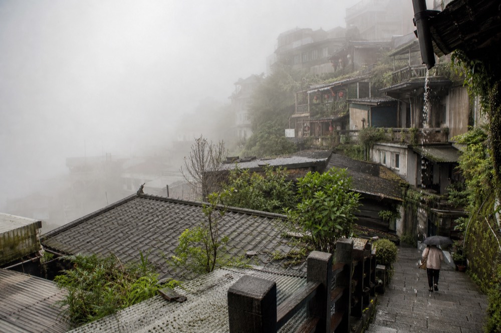 Fog drifting between the rooftops of a hillside town above the sea