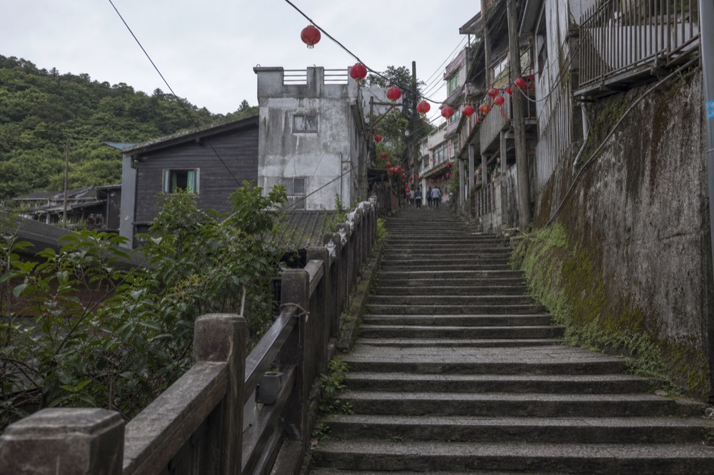A steep stone staircase between old buildings with lanterns strung overhead and no people