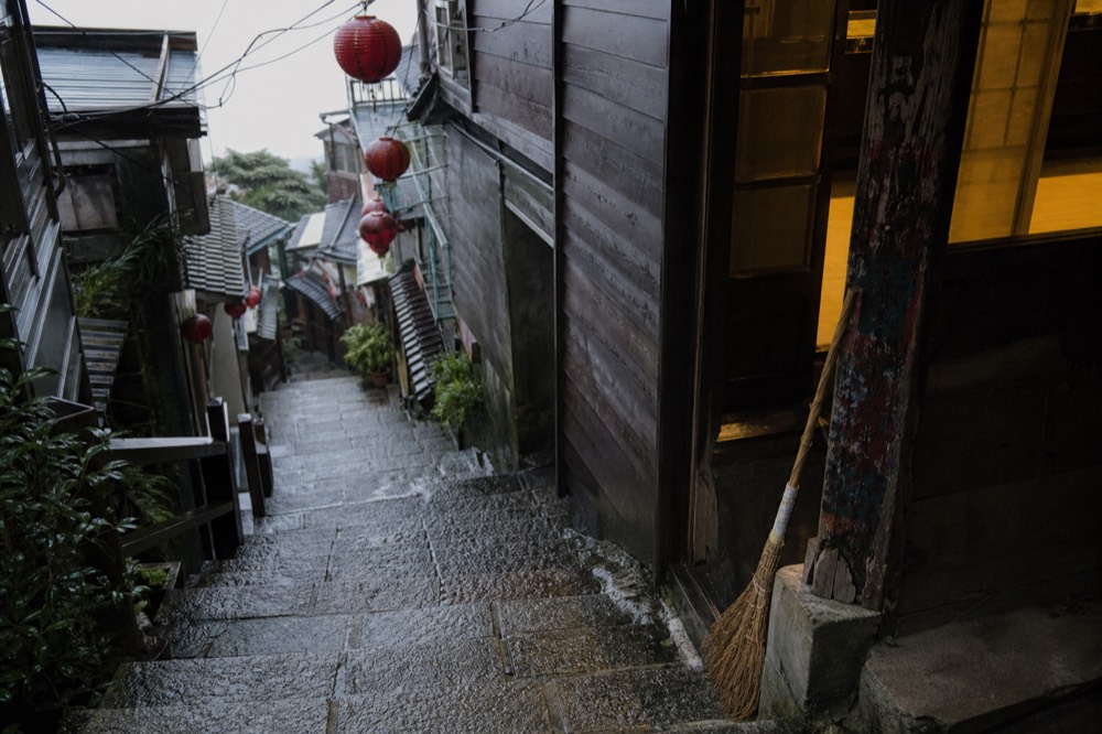 Steep stone steps between old wooden buildings with red lanterns hanging overhead in a hillside town