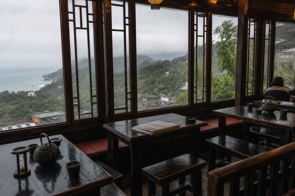 Wooden teahouse interior with low tables, tea sets and lattice windows overlooking a coastal hillside