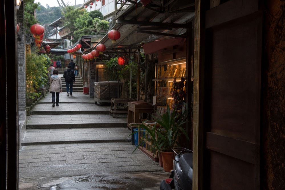 Old street lined with souvenir stalls and hanging lanterns stretching up a hillside in daylight