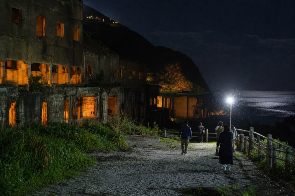Illuminated ruins of a former mining structure on a dark hillside above the sea at night