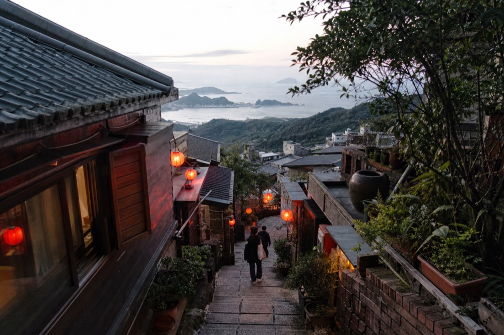 Coastal hillside town seen from above with rooftops descending toward the sea in late afternoon light