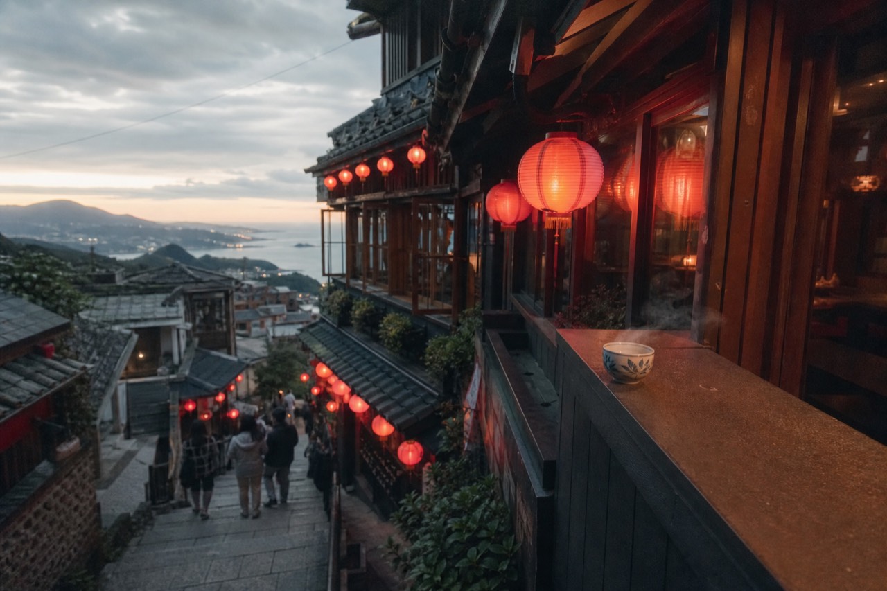 Red lanterns glowing along a steep stone lane of old teahouses on a hillside at dusk