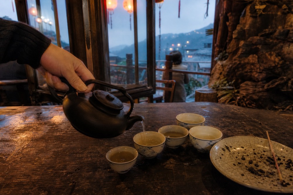 Teapot being poured into small cups on a wooden table