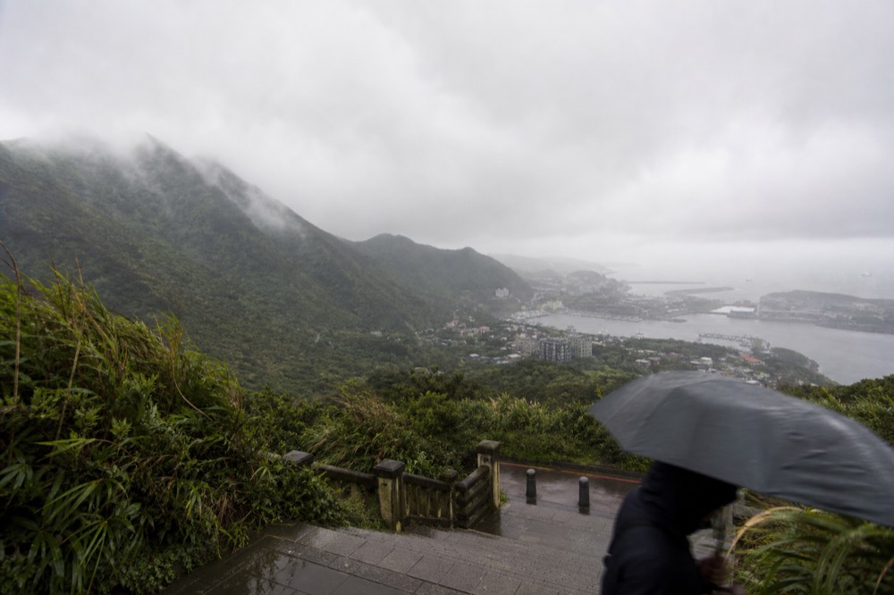 Rain clouds rolling over green coastal mountains with a grey harbour in the distance