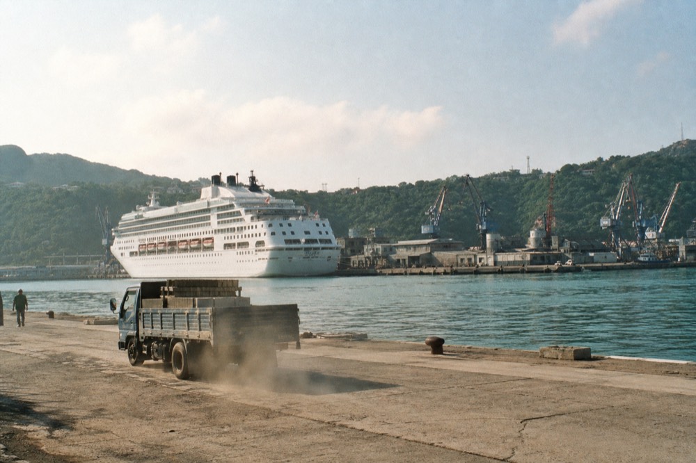 A large cruise ship docked at a harbour terminal between hills