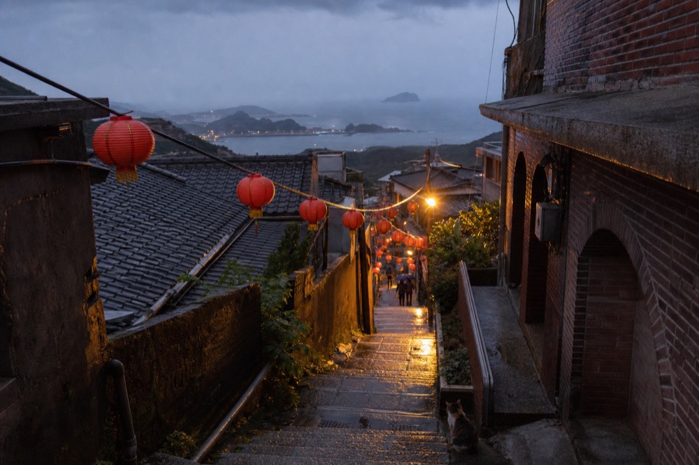 A hillside old street with red lanterns strung across narrow lanes above the sea