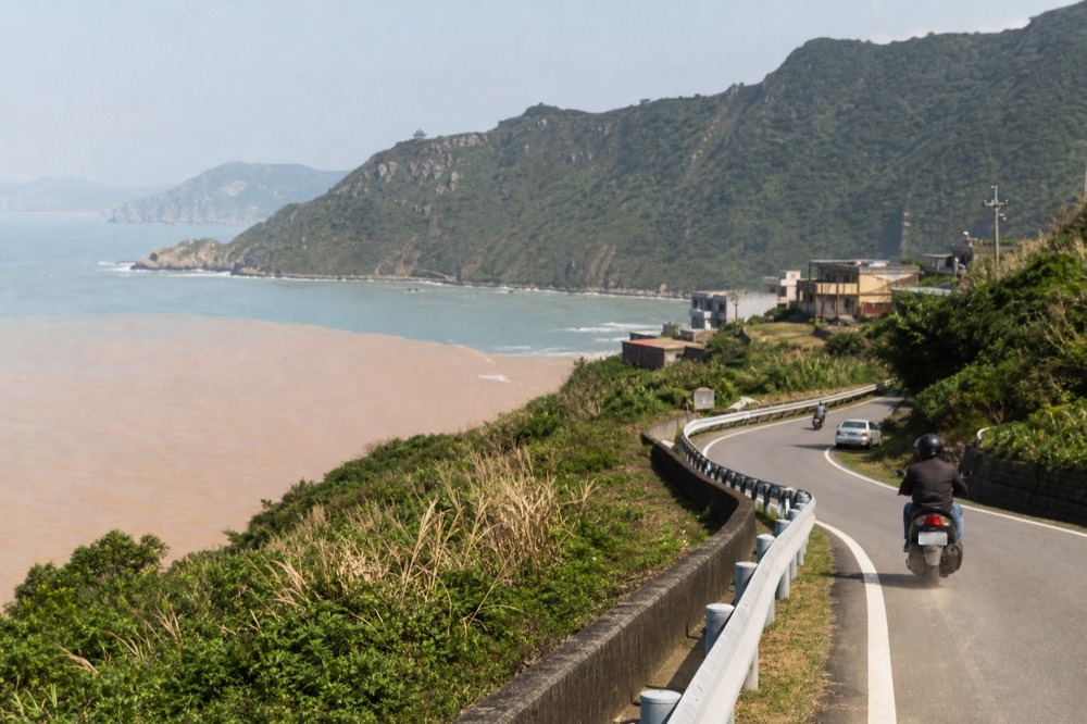 A coastal road curving along a headland with the sea on one side and green slopes on the other