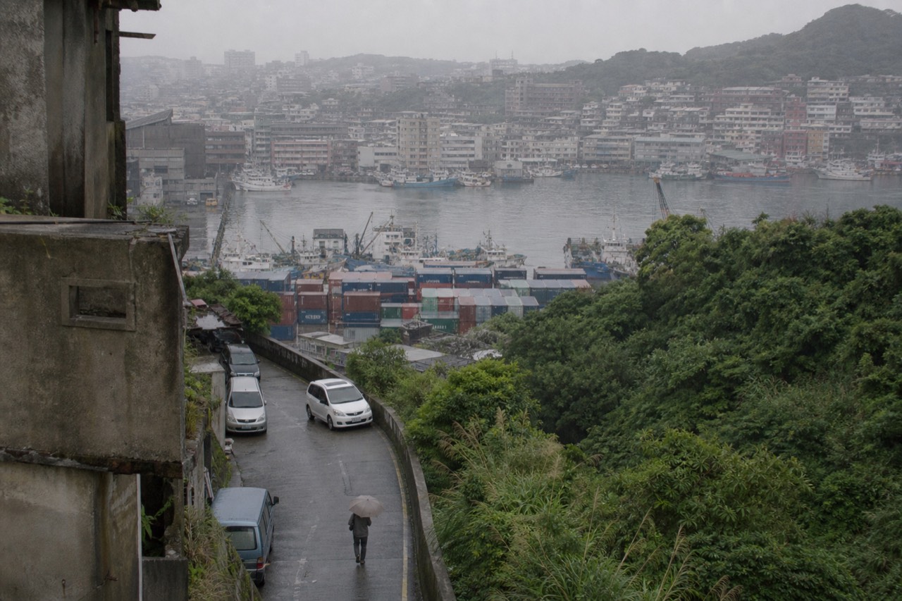 Harbour city buildings beneath steep green hills on Taiwan's north coast, with grey sea beyond