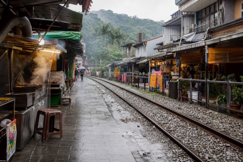 A village street in a narrow valley with railway tracks running along the middle between food stalls