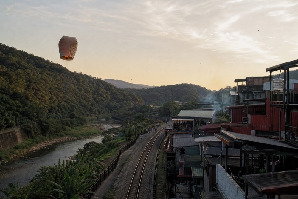 A sky lantern rising above a river valley in the late afternoon