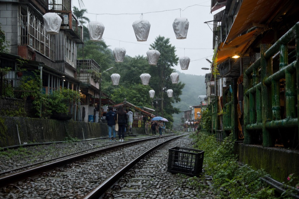 A quiet village street with lanterns hanging above empty railway tracks in morning light