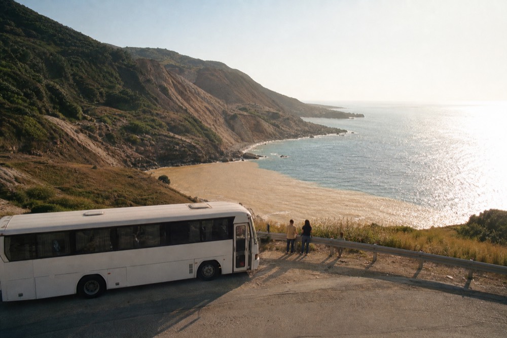 A tour coach parked on a coast road above a blue sea in the late afternoon
