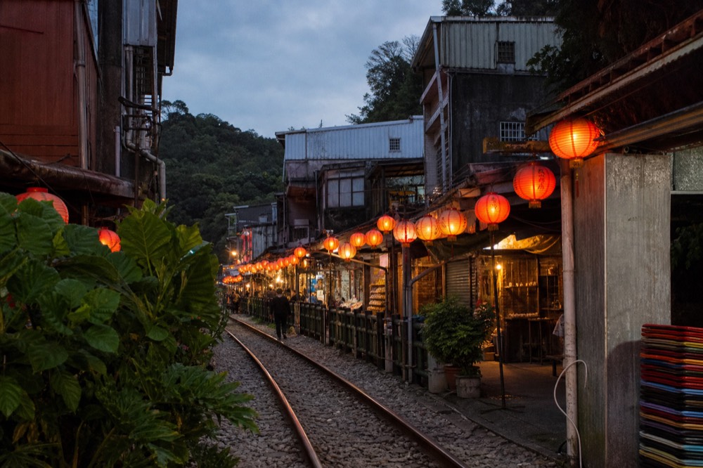 Red lanterns glowing above a village street at dusk with hills behind