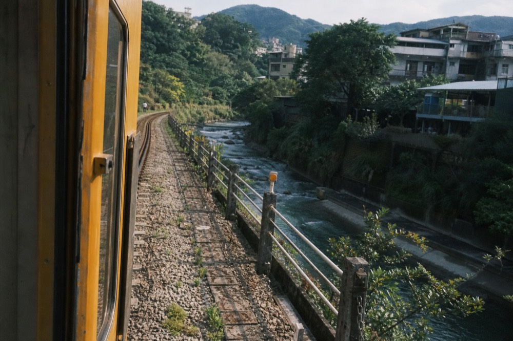 A single-track railway line curving along a river between steep green hills in a narrow valley