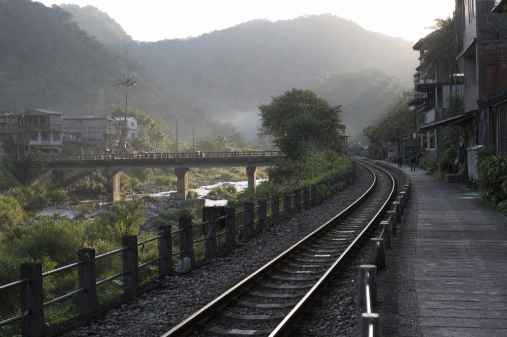 A single-track rural railway line curving through green hills in northern Taiwan