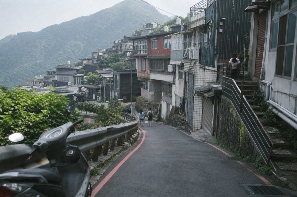 A winding mountain road climbing through buildings toward a hillside town in northern Taiwan