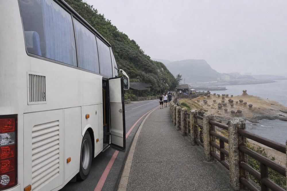 A tour coach parked on a coastal road beside rock formations and the sea