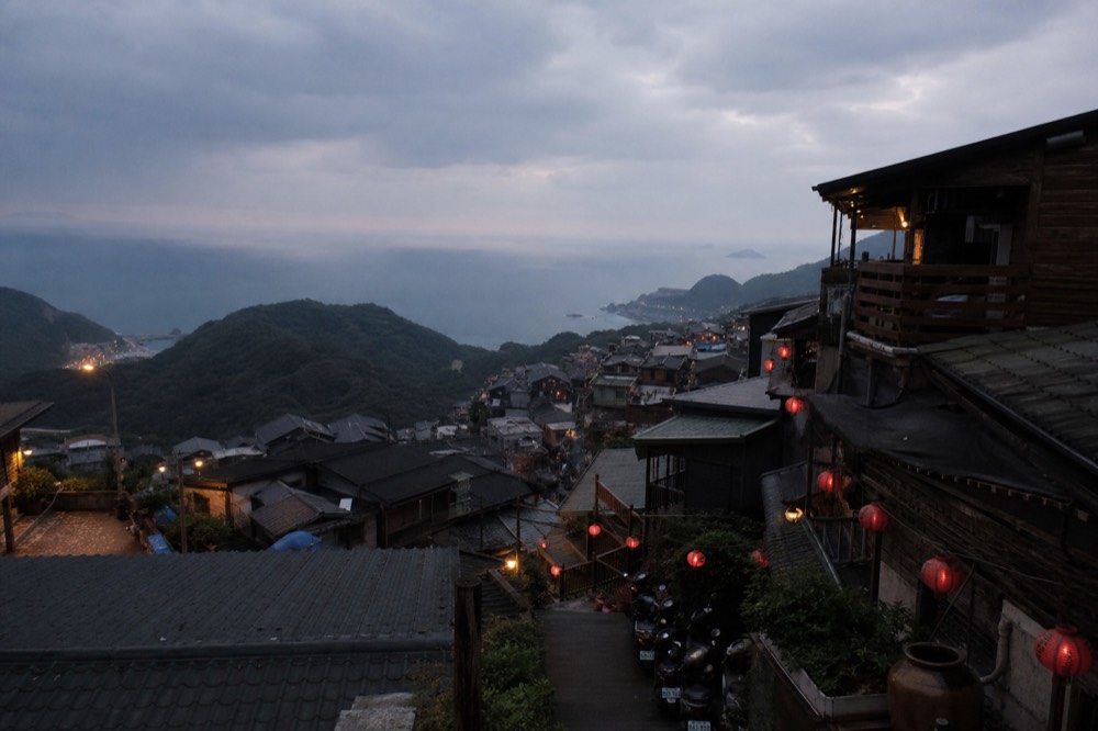 Lanterns and rooftops of a hillside town seen from a lookout at dusk