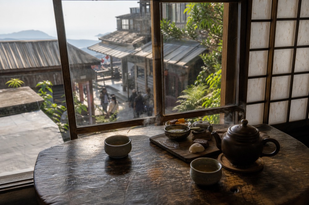 A tray of small tea snacks and a clay teapot on a wooden table in a hillside teahouse