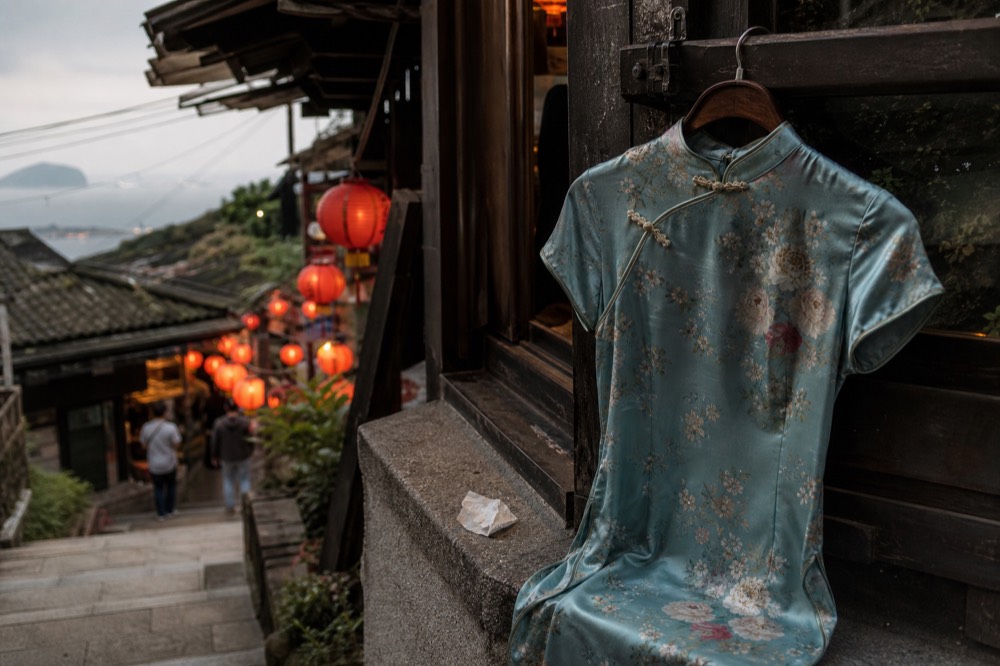 A traditional Chinese dress on a wooden hanger against the backdrop of a lantern-lit lane