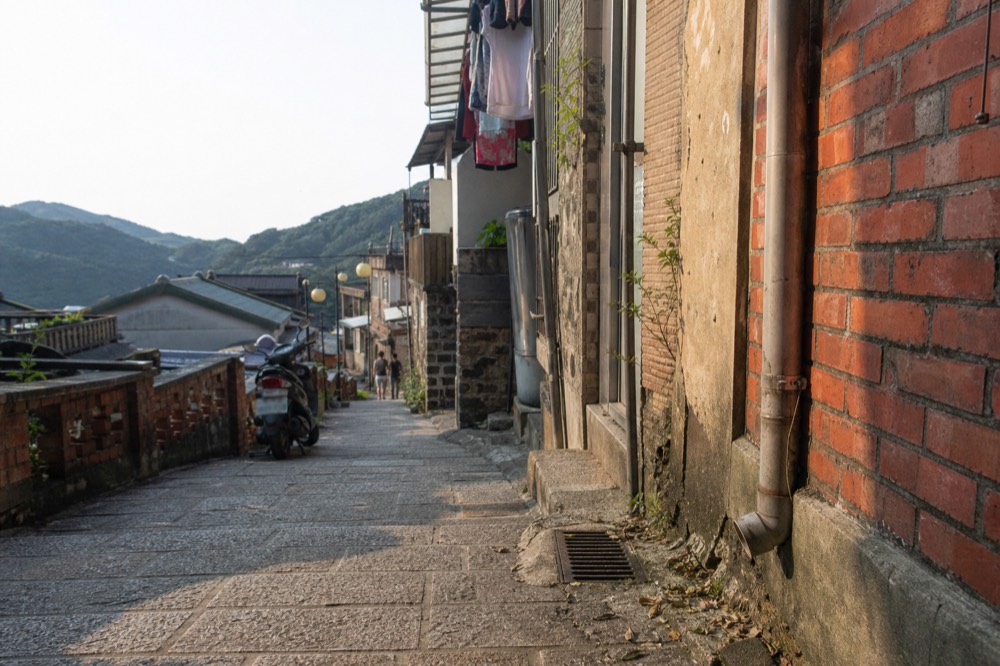 A quiet stone lane between old houses on a Taiwanese hillside in soft afternoon light