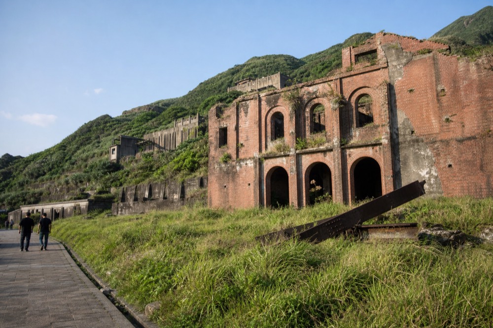 A disused mining building with tall brick arches standing on a green hillside