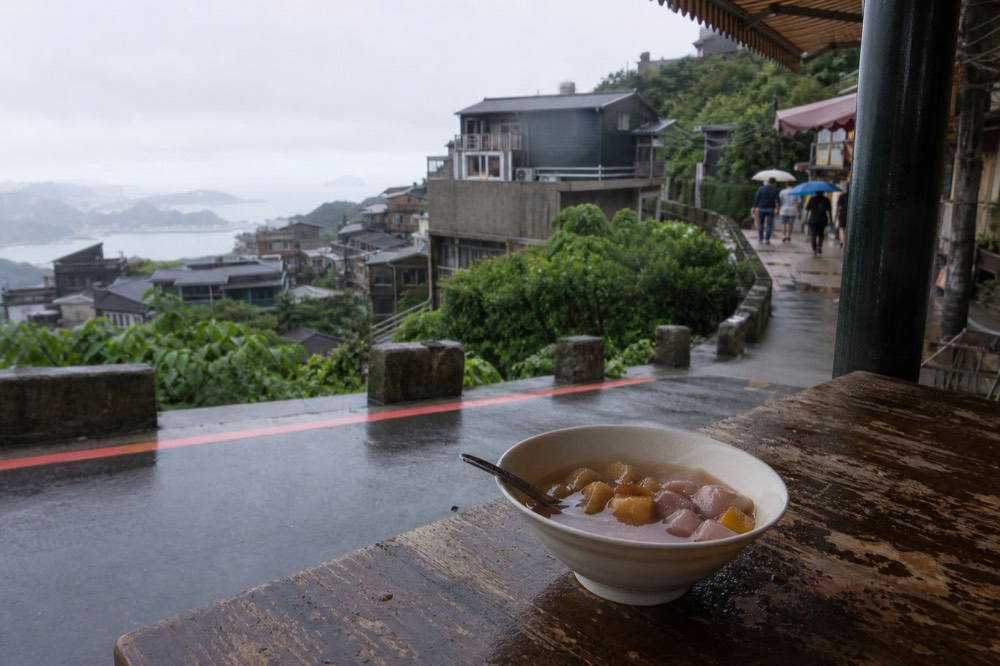 A bowl of taro balls in sweet soup on a wooden table with a view of Jiufen's hillside