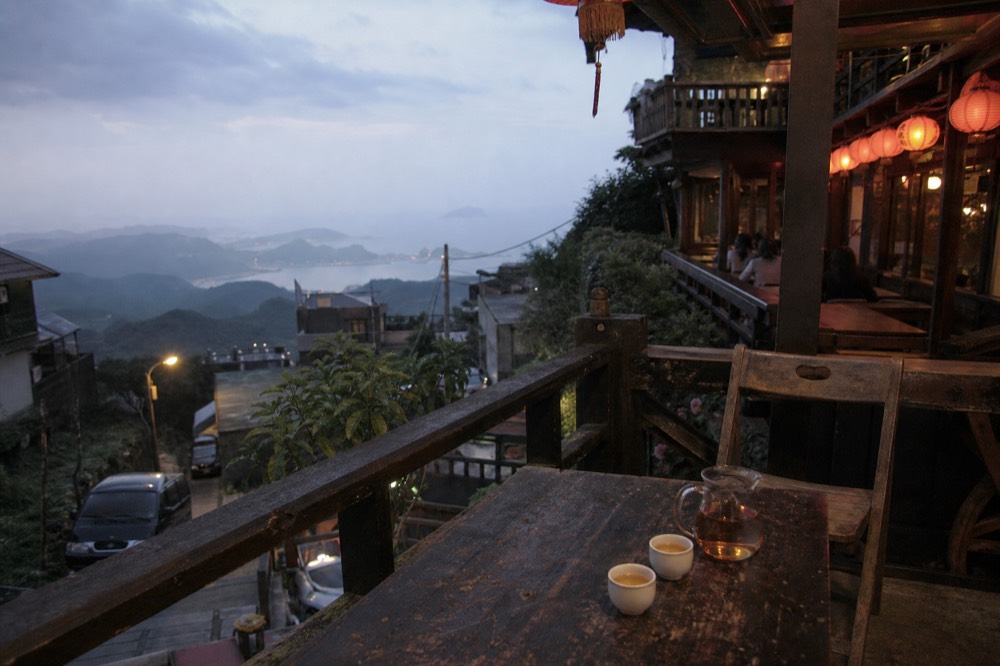 The red-lanterned terrace of A-Mei Tea House at dusk, with tea cups on a wooden table