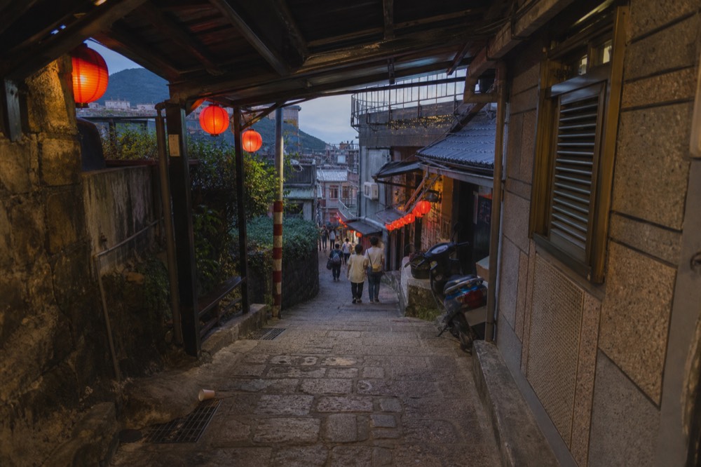 Jiufen Old Street at dusk with red lanterns glowing and a few visitors walking