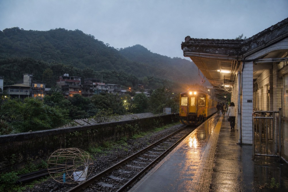 A rural branch line railway platform at dusk with a single lit train