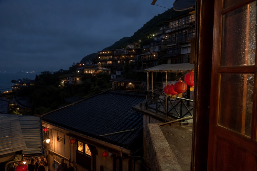 A dark hillside town with scattered warm window lights above a night sea