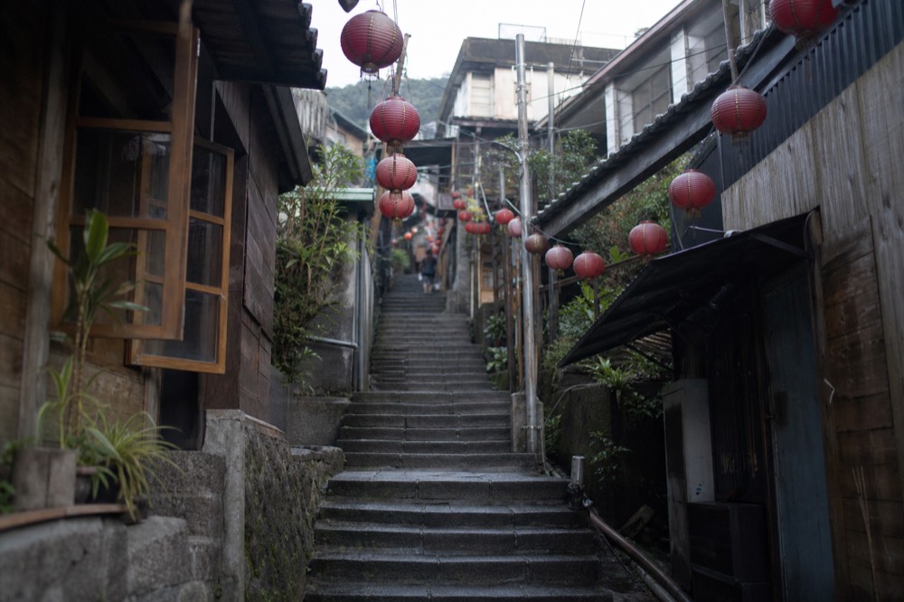 A narrow stepped lane between old shopfronts with hanging red lanterns