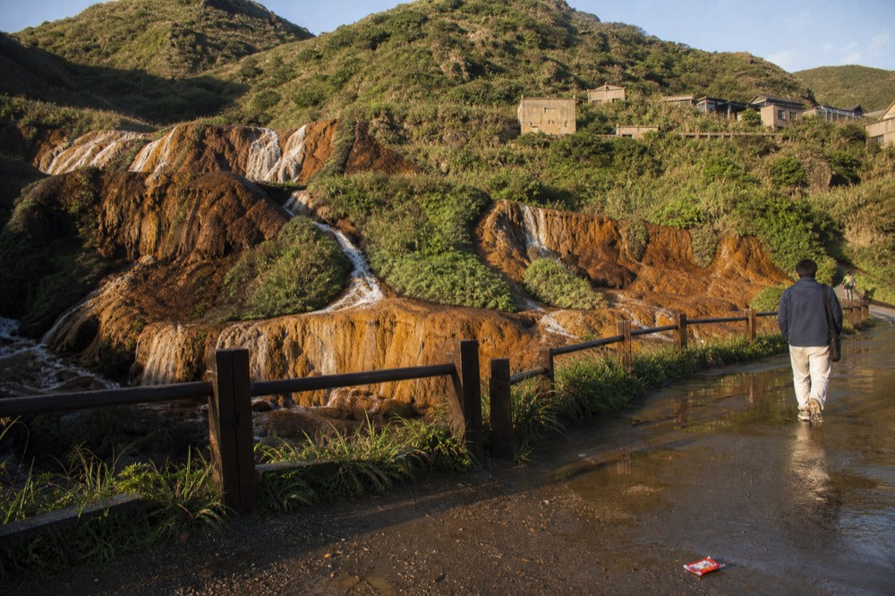 Waterfall of orange-stained water cascading over rock steps near an old mining area