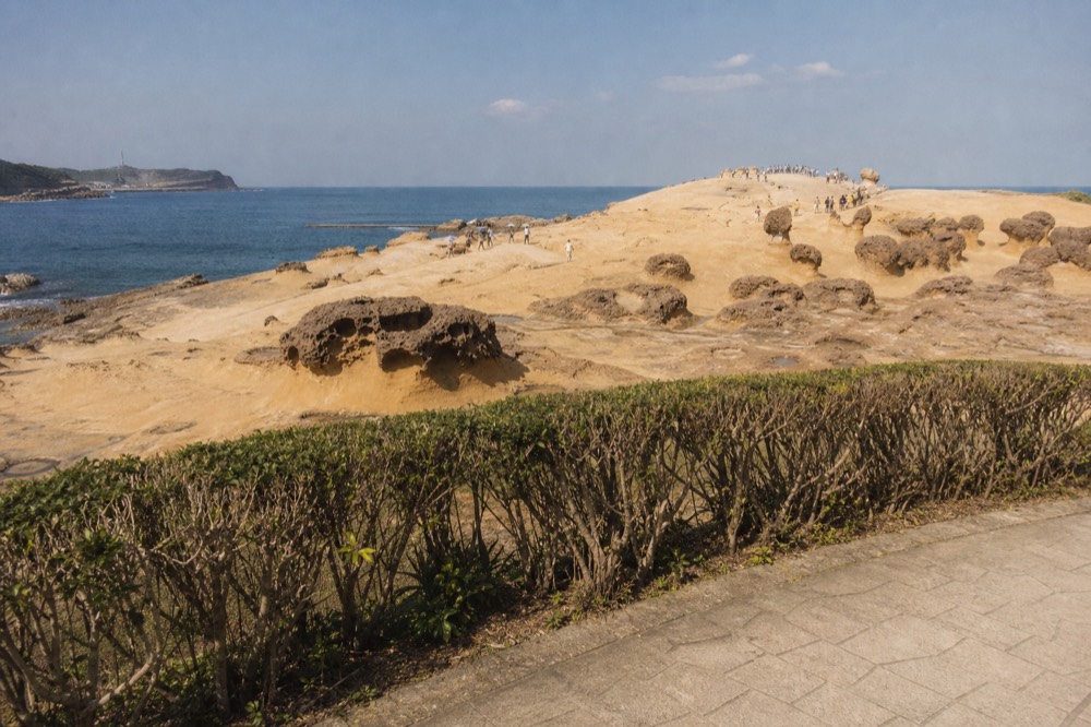 Wide view of a sandstone cape extending into open sea under a bright sky