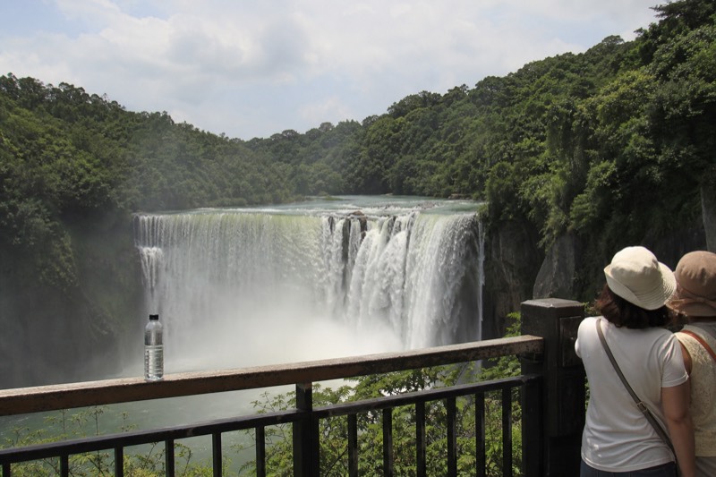A tall thin waterfall dropping between green cliffs in northern Taiwan, visitors at the viewing platform nearby