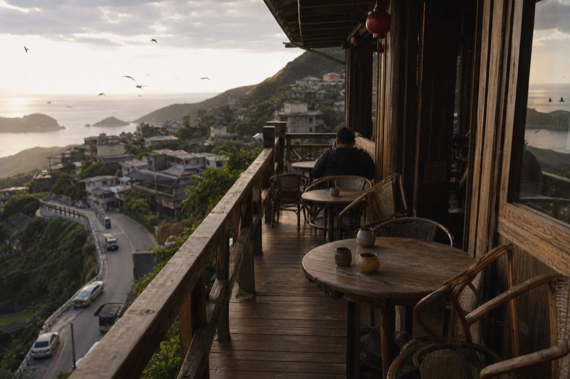 A wooden teahouse terrace in Jiufen looking out over the sea, small tables set for tea on the balcony